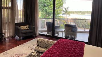 A modern room with a large sliding glass door leading to a balcony. The room features a sofa, a small armchair, and a bed with a red blanket.