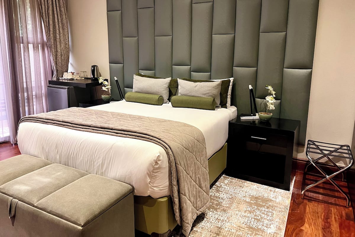 A modern bedroom with a large bed, a padded headboard, bedside tables, a bench, and a view of the outdoors.