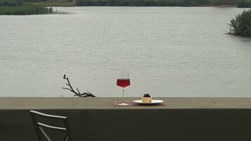 Una silla y una mesa con una copa de vino tinto y un postre junto a un lago.
