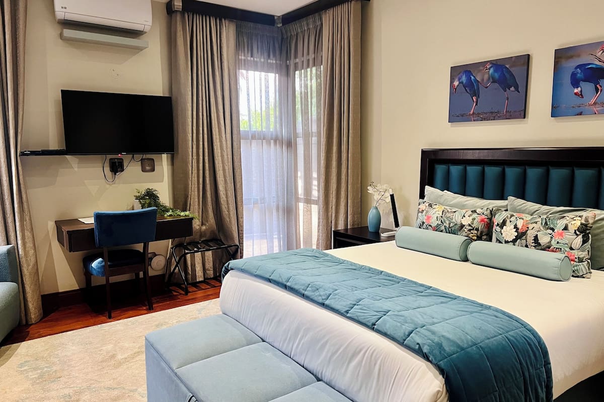 A hotel room with a bed, a desk, a chair, a TV, and artwork on the wall.