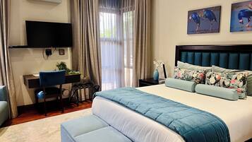 A hotel room with a bed, a desk, a chair, a TV, and artwork on the wall.