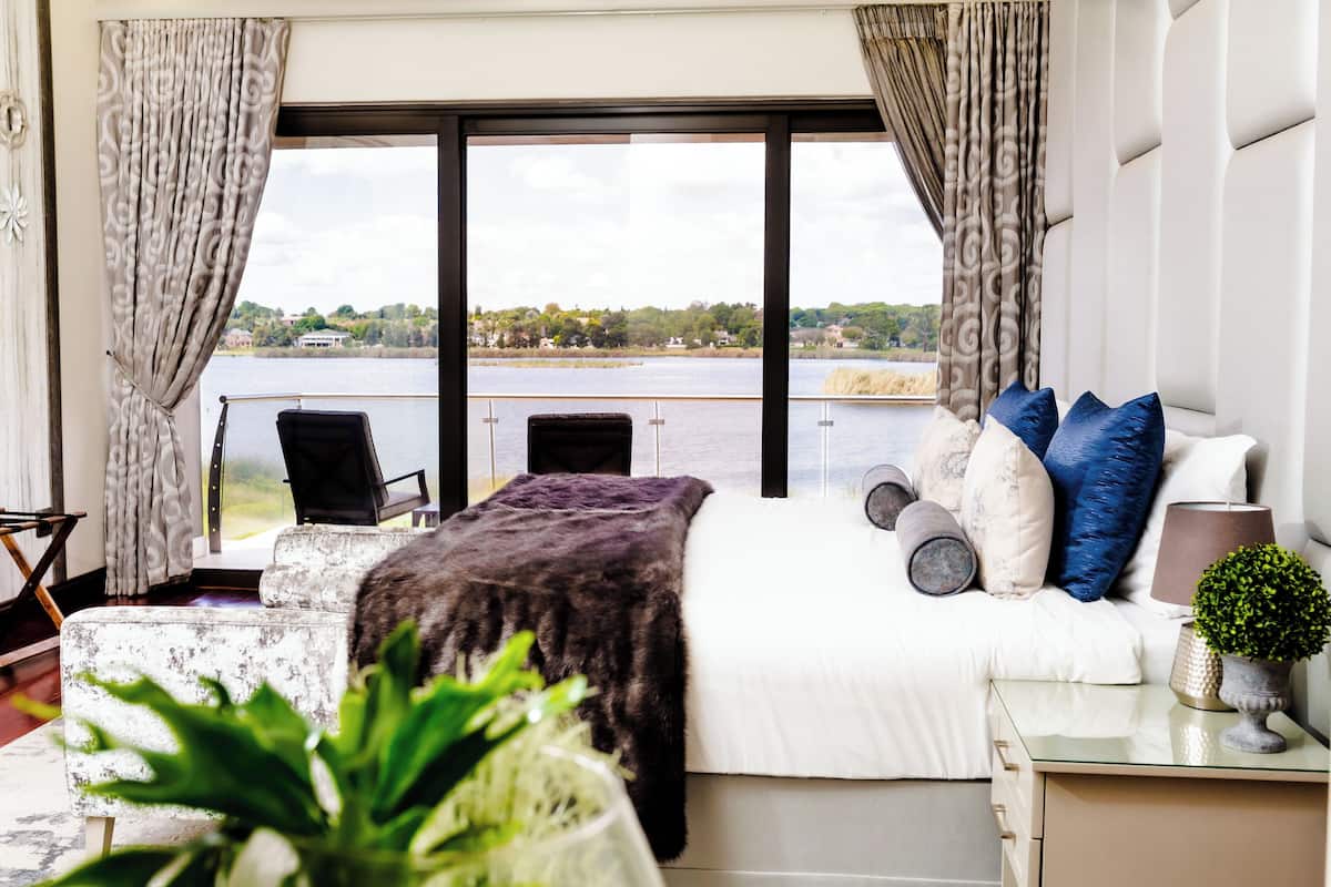 A bedroom with a large bed, a view of a lake, and a balcony with a chair.