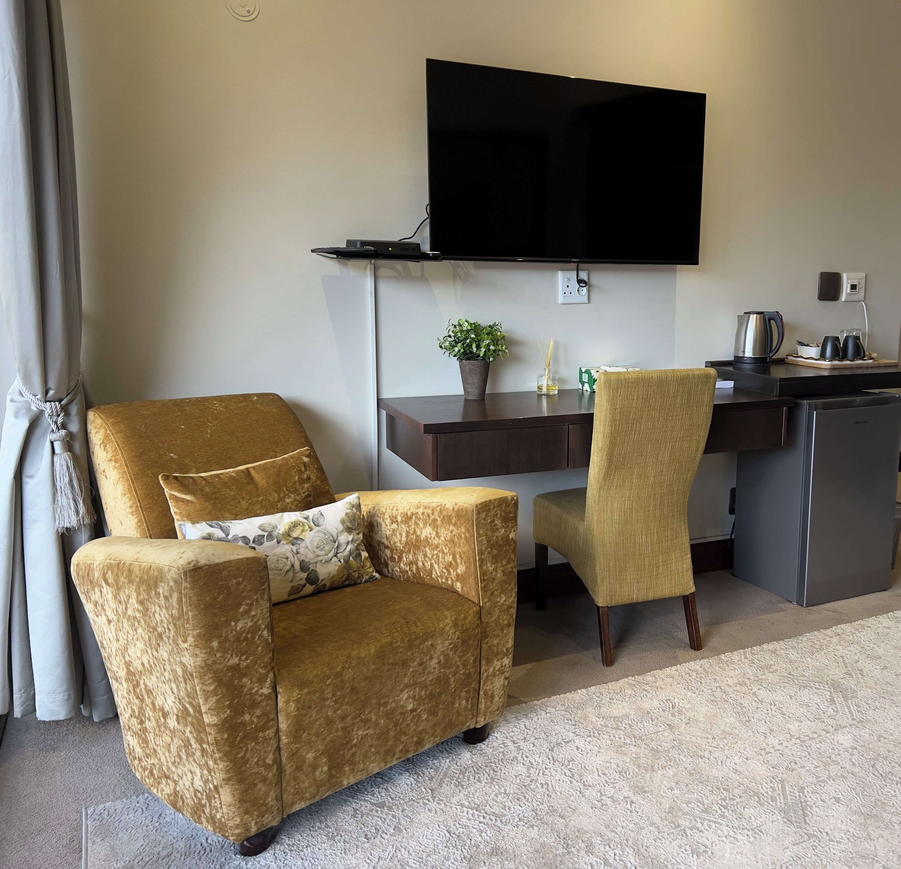 Ein modernes Hotelzimmer mit einer Couch, einem Sessel, einem Schreibtisch, einem Flachbildfernseher, einer Kaffeemaschine und einer kleinen Pflanze.