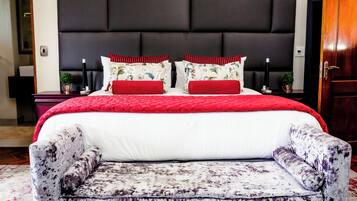 Un dormitorio con una cama grande, cabecera, mesitas de noche y un sillón con estampado.
