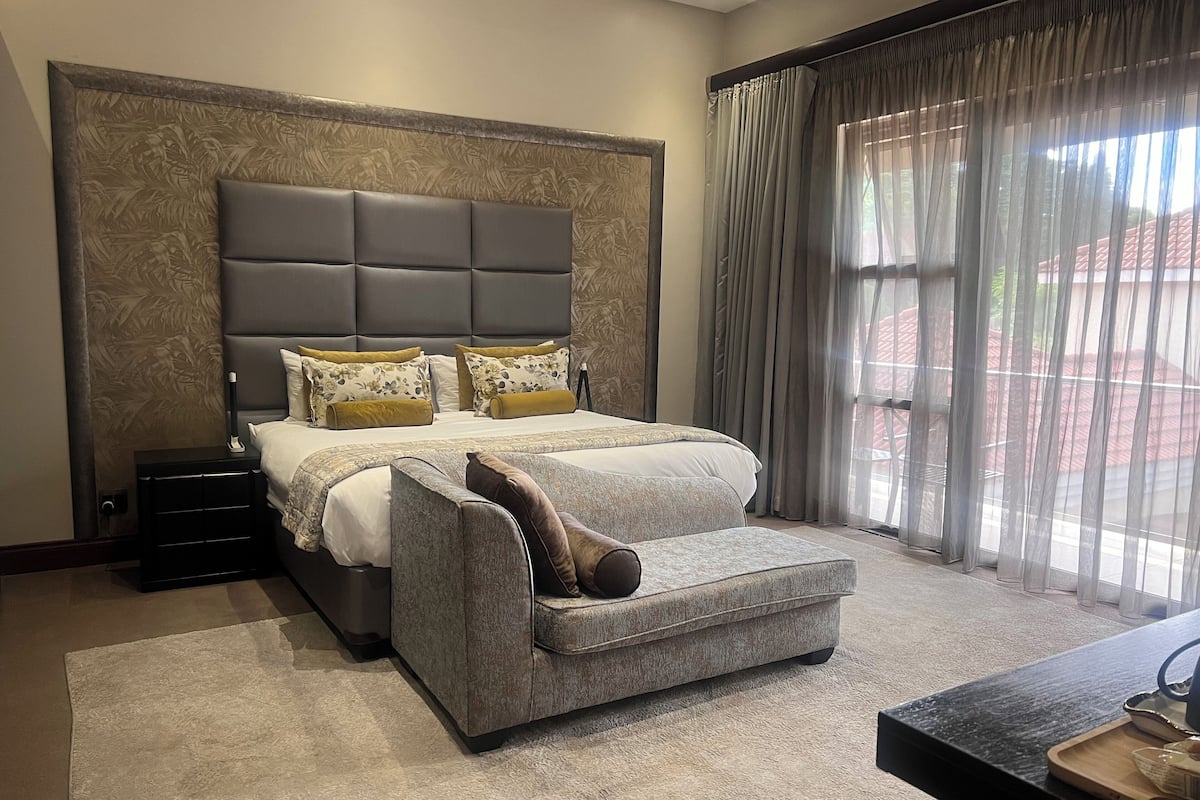 A bedroom with a large bed, a nightstand, a sofa, and a window with curtains.