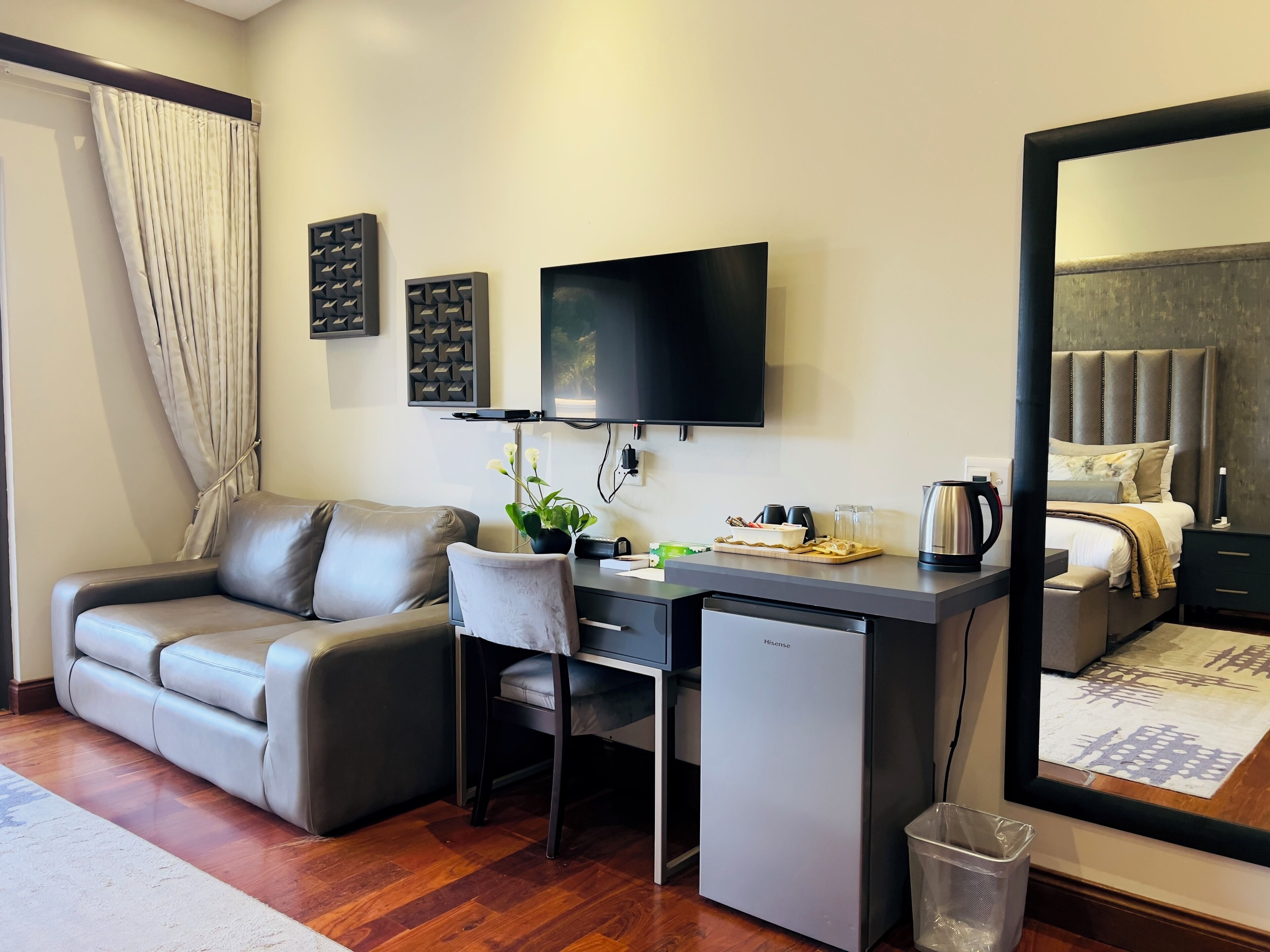 A hotel room with a sofa, desk, chair, television, and a bed with a headboard.