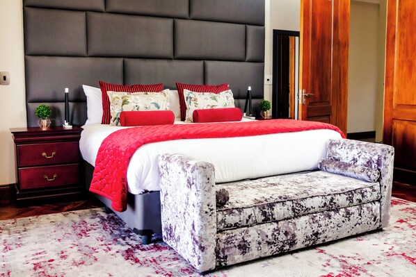 A bedroom with a large bed, a nightstand, a bedside table, and a wooden door.