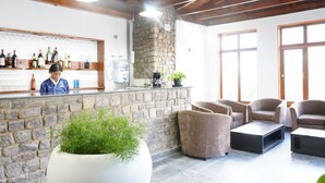 Un espace bar avec un mur en pierre, un plafond en bois et des sièges, agrémenté d’une grande plante en pot.