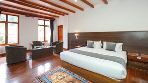 Une chambre spacieuse avec un grand lit, des poutres apparentes au plafond, un coin salon avec un canapé et un fauteuil, et de grandes fenêtres laissant entrer la lumière naturelle.
