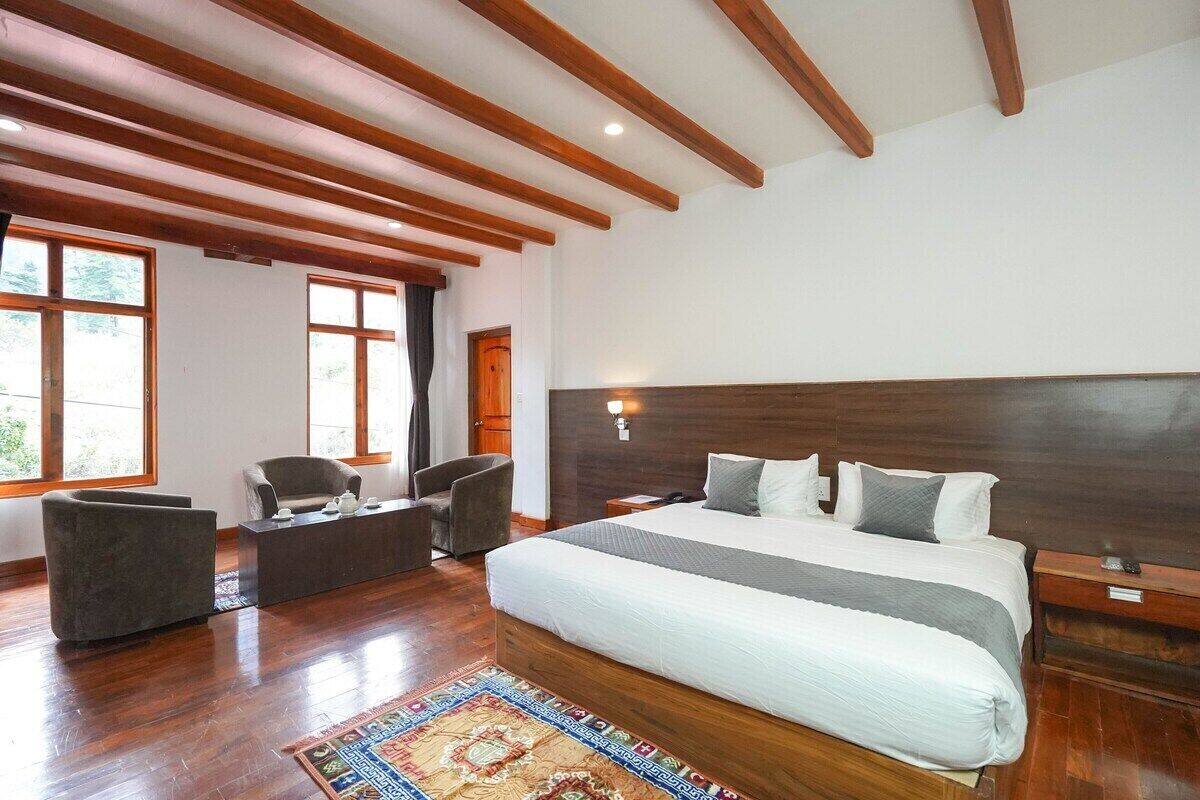Un dormitorio amplio con una cama grande, vigas de madera en el techo, un rincón de descanso con sofá y sillón, y ventanas grandes que aportan luz natural.