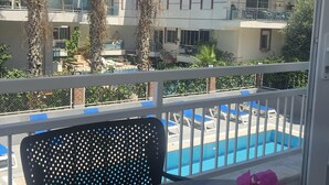 Un balcón con piscina, palmeras y un edificio con balcones al fondo.