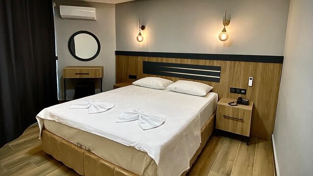 Un dormitorio moderno con una cama grande, mesitas de noche, un espejo redondo e iluminación en la pared.