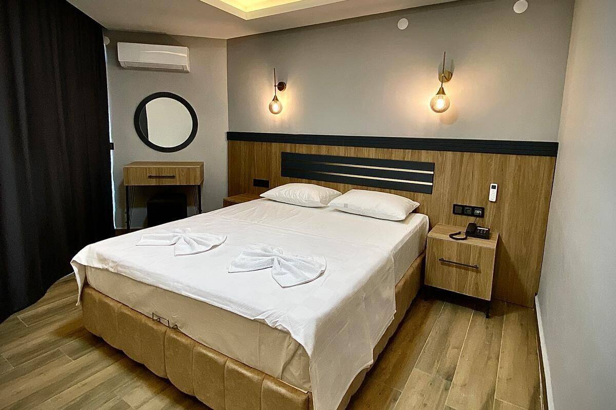 A modern bedroom with a large bed, bedside tables, a round mirror, and wall-mounted lights.