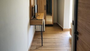 Un pasillo con suelo de madera, un escritorio con ordenador, una lámpara en el techo y una puerta.
