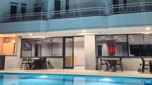 Un hotel de varios pisos con piscina, balcones y una zona de bar.