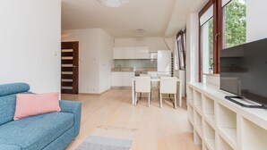 Ein modernes Wohnzimmer mit einem blauen Sofa, einem Fernseher auf einem weißen Schrank und einer Küche im Hintergrund.