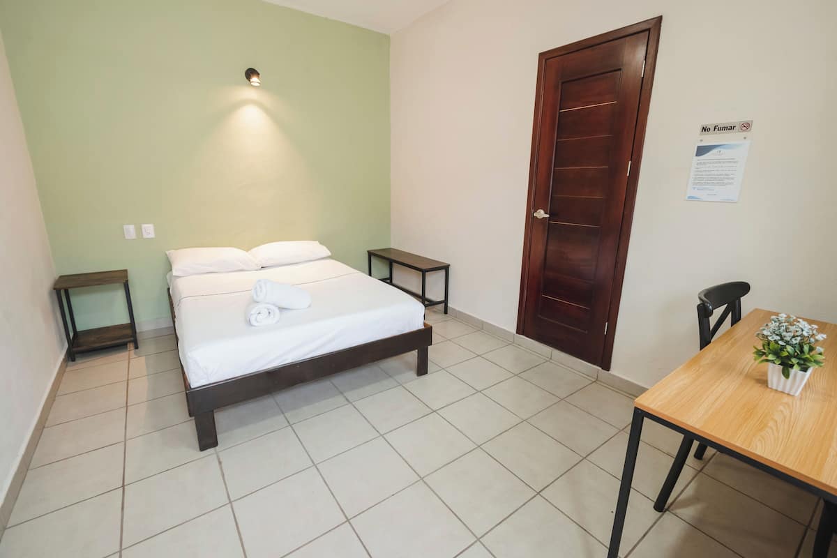 A room with a bed, a small table, a chair, and a door.
