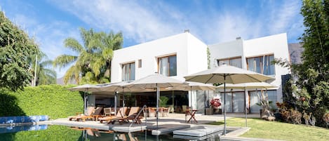 Ein modernes Haus mit Swimmingpool, Sitzgelegenheit im Freien und einem gepflegten Garten.