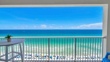 Een balkon met uitzicht op een strand, een tafel met een plant en blauwe stoelen.