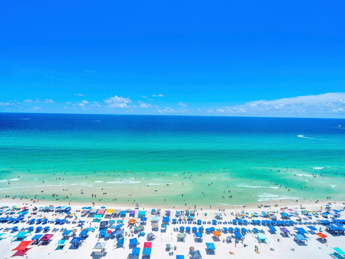 Een strand met tal van ligbedden en parasols, een heldere blauwe lucht en een rustige zee.