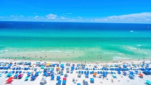 A beach with numerous sun loungers and umbrellas, a clear blue sky, and a calm sea.