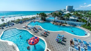 A pool area with multiple swimming pools, lounge chairs, and a view of the beach.
