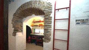 A narrow hallway with a stone archway leading to a kitchen area. A red ladder is leaning against the wall to the right. - 340 Livingtarifa Warhol (Tarifa)
