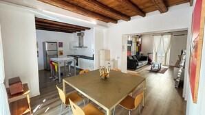 Un espai de vida ampli amb sostre de fusta, taula de menjador amb cadires, cuina al fons i un sofà a la sala adjacenta.