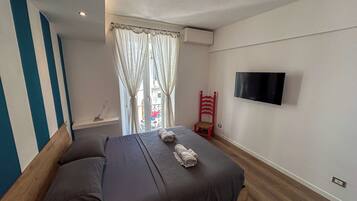 Ein Schlafzimmer mit einem Bett, einem roten Sessel, einem Fernseher und einem Fenster mit Vorhängen.