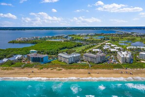 An aerial view of a coastal resort with beachfront properties, a marina, and a bridge in the background. - Beautiful top floor condo with stunning lake & river views on Hutchison Island (Stuart)