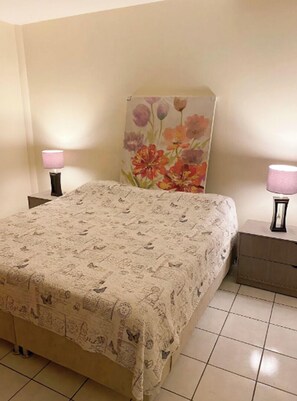 A bedroom with a floral headboard, a patterned bedspread, two bedside lamps, and a small bedside table. - New Apt in GDL Near Cathedral  (Guadalajara)