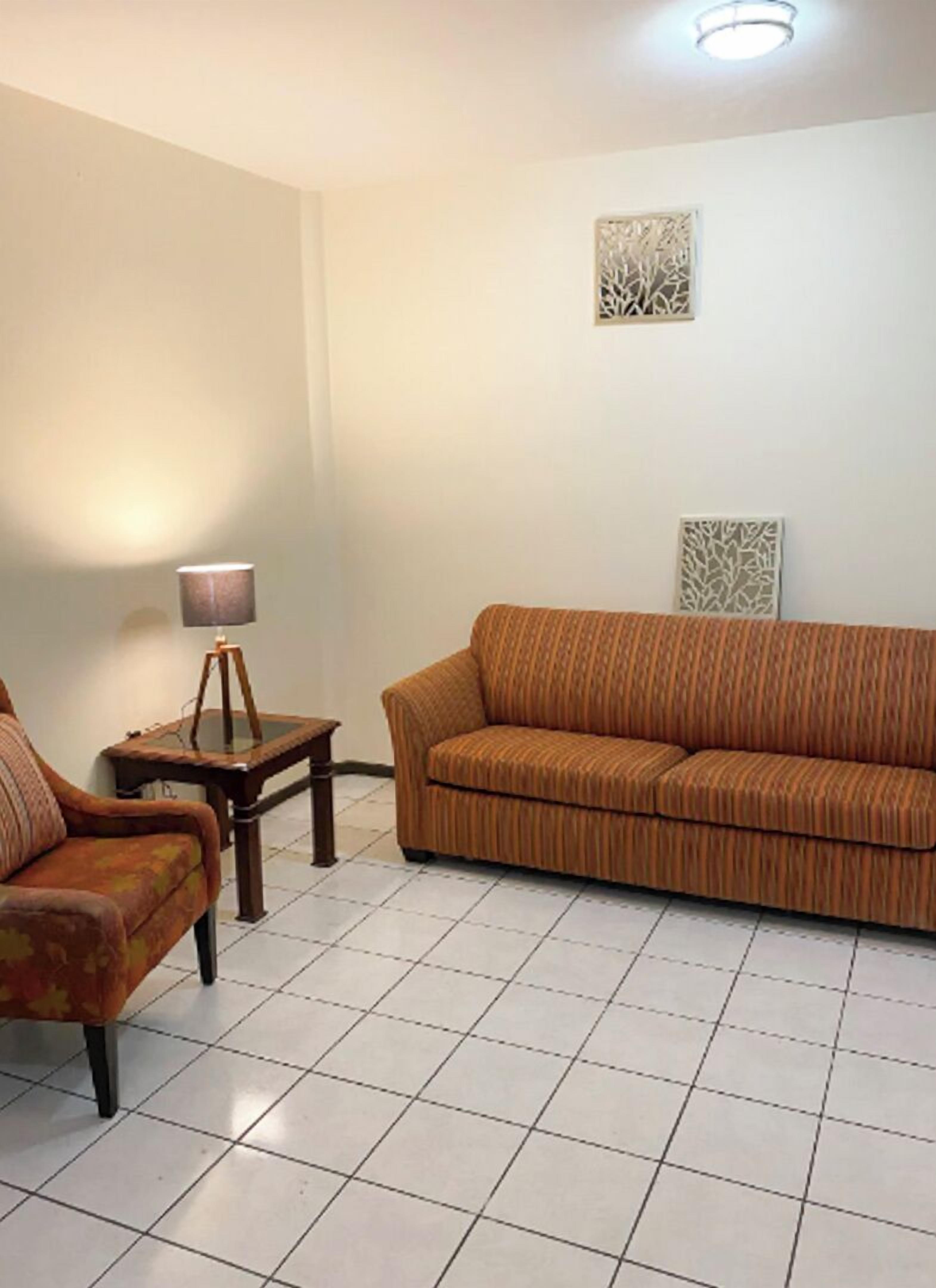 A living room with a sofa, a chair, a small table with a lamp, and decorative wall art.