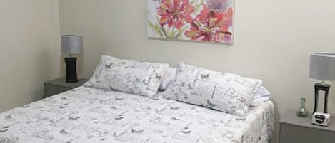 A bedroom with a bed, two nightstands, a wall-mounted painting, and a tiled floor.