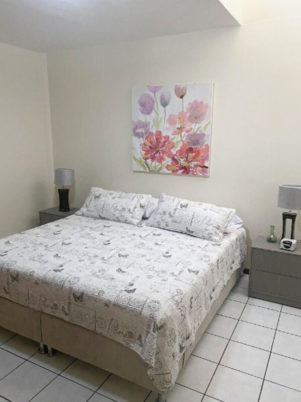 A bedroom with a bed, two nightstands, a wall-mounted painting, and a tiled floor. - New Apt in GDL Near Cathedral (Guadalajara)