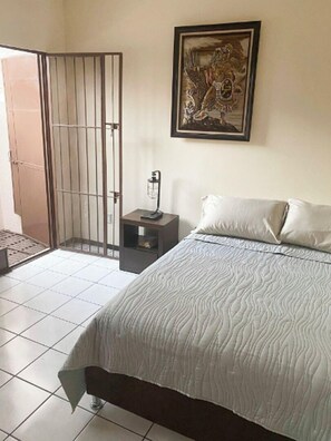 A bedroom with a bed, a nightstand, a framed artwork, and a barred door. - New Apt in GDL Near Cathedral  (Guadalajara)