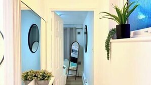 A hallway with a mirror, potted plants, and a door leading to another room. - Cozy home with a garden walkable distance to the heart of Hertford   (Hertford)