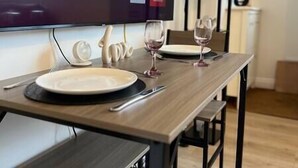 A dining table set with plates, cutlery, and wine glasses, with a television mounted on the wall behind.