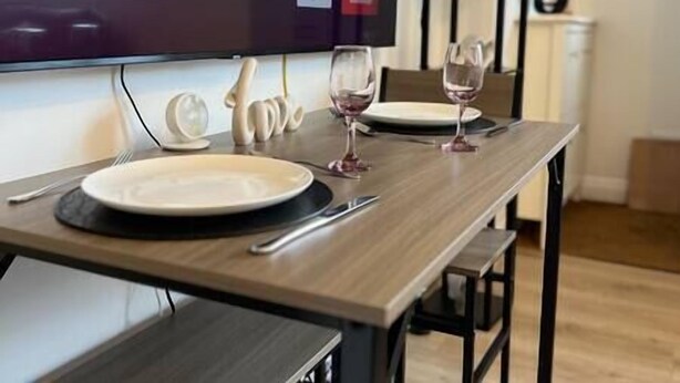 A dining table set with plates, cutlery, and wine glasses, with a television mounted on the wall behind. - Cozy home with a garden walkable distance to the heart of Hertford   (Hertford)
