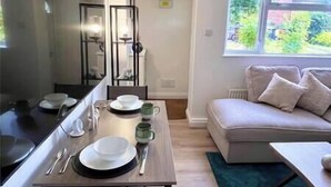 A dining area with a table set for four, a sofa, and a window with a view of greenery. - Cozy home with a garden walkable distance to the heart of Hertford   (Hertford)