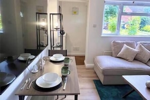 A dining area with a table set for four, a sofa, and a window with a view of greenery.