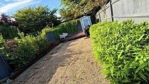 A garden pathway leading to a white door, surrounded by lush greenery and a wooden fence.