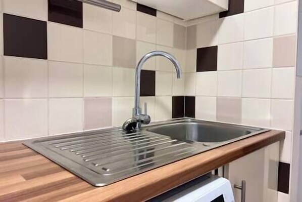 A kitchen with a stainless steel sink, a wooden countertop, and a tiled backsplash.