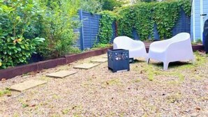A garden with a blue fence, white plastic chairs, and a shed.