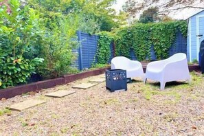 Un jardín con valla azul, sillas de plástico blanco y un cobertizo.
