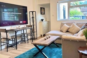 Una sala de estar con televisor, sofá, mesa de centro y comedor.
