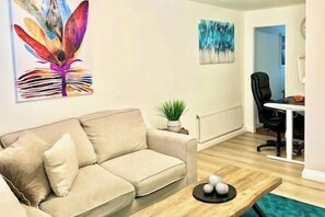 A living room with a beige sofa, a coffee table, and a painting on the wall. - Cozy home with a garden walkable distance to the heart of Hertford   (Hertford)