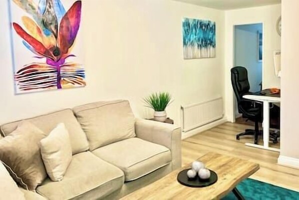 Un salón con un sofá beige, una mesa de centro y un cuadro en la pared.