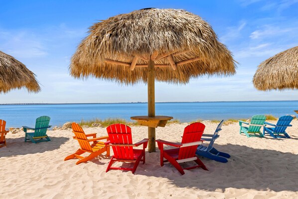 A beach with colorful Adirondack chairs and a thatched umbrella.