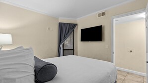 Een hotelkamer met een bed, een flatscreen televisie aan de muur, een raam met gordijnen en een deur.