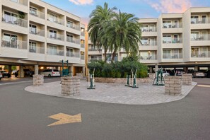 Ein mehrstöckiges Hotel mit Balkonen, einem zentralen, begrünten Innenhof mit Palmen und einem Parkplatz.